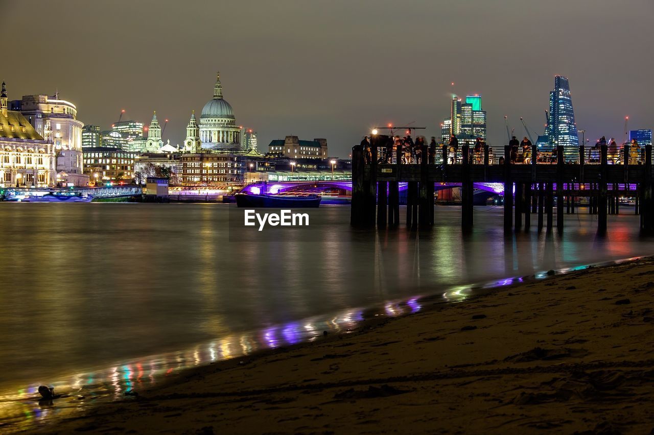 Thames river by illuminated st paul cathedral against sky at night