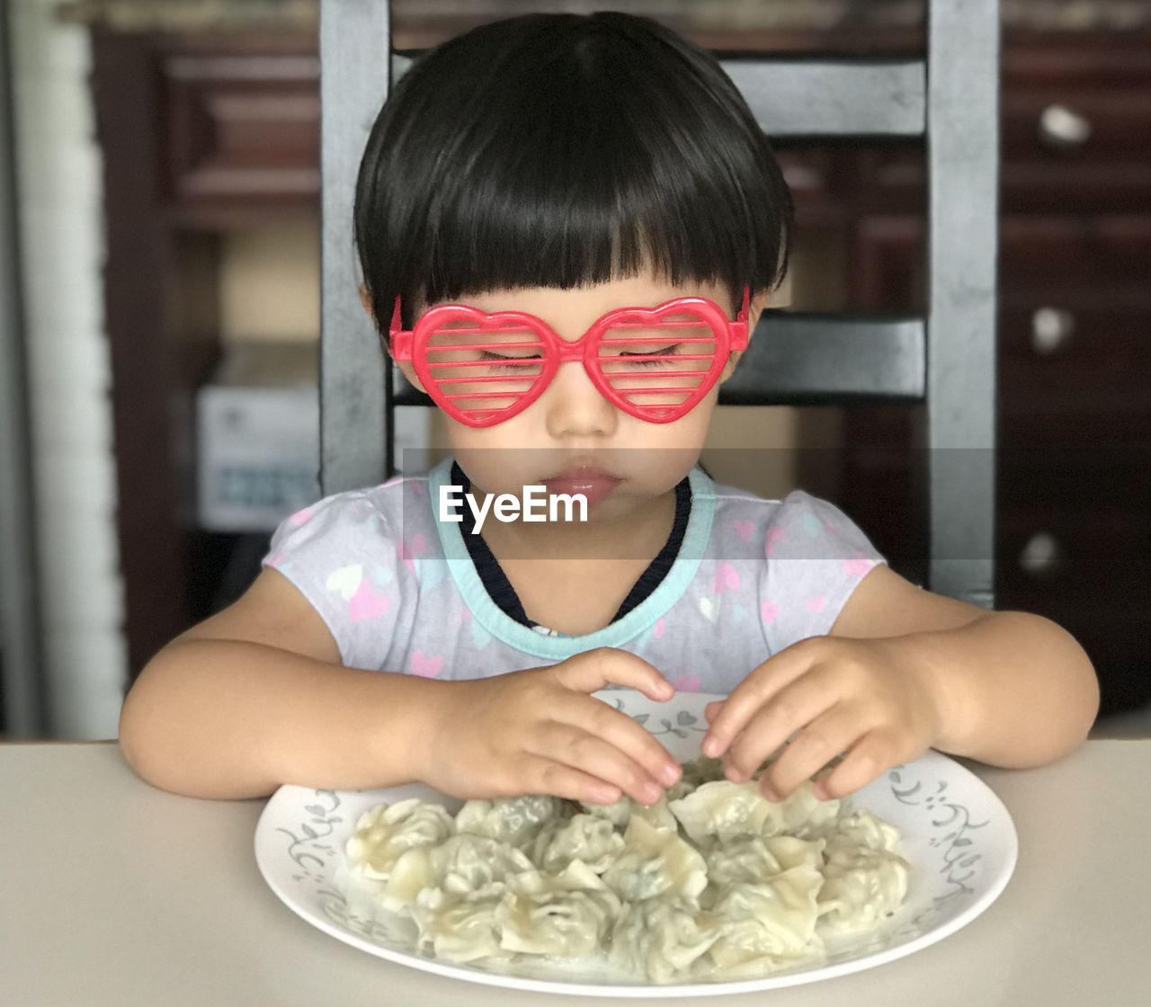 Cute girl wearing sunglasses eating food at home