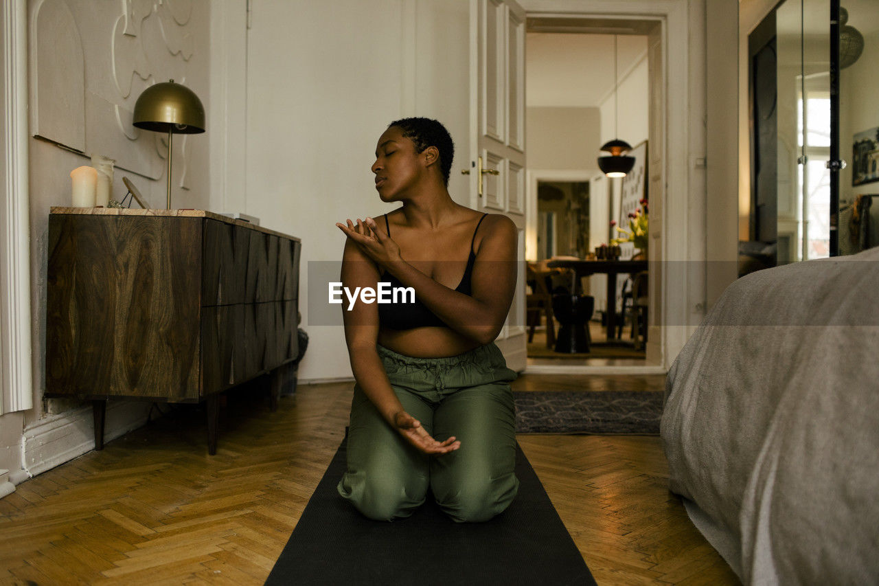 Young woman with eyes closed practicing relaxation exercise in bedroom at home