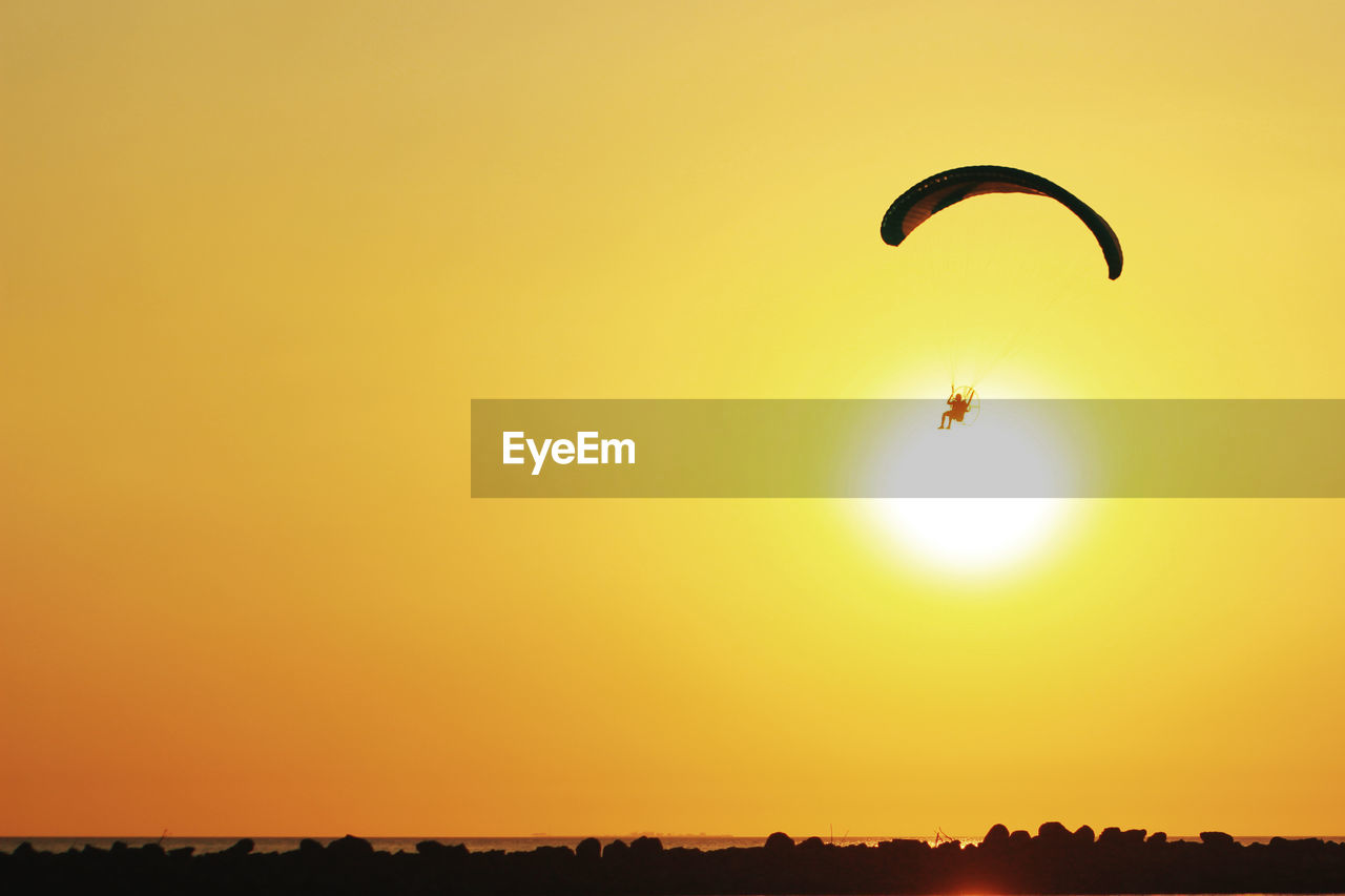 Person powered paragliding over sea against clear sky during sunset