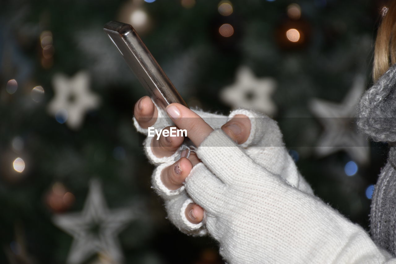 Midsection of woman using mobile phone while standing by christmas tree