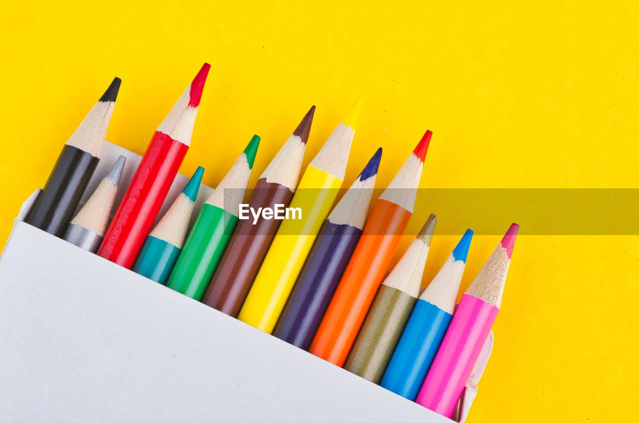 Close-up of colored pencils over yellow background