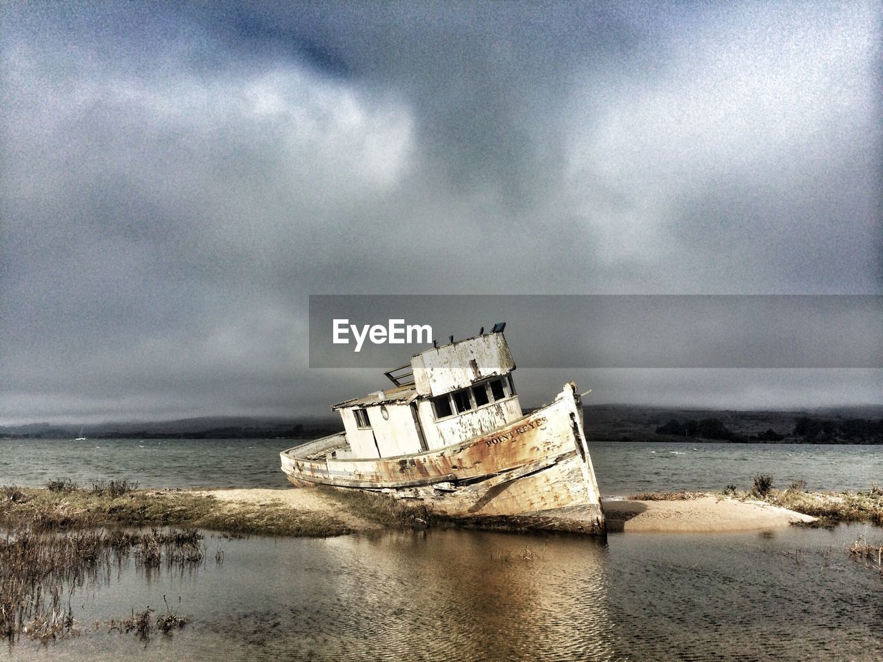 Abandoned boat moored in beach against cloudy sky