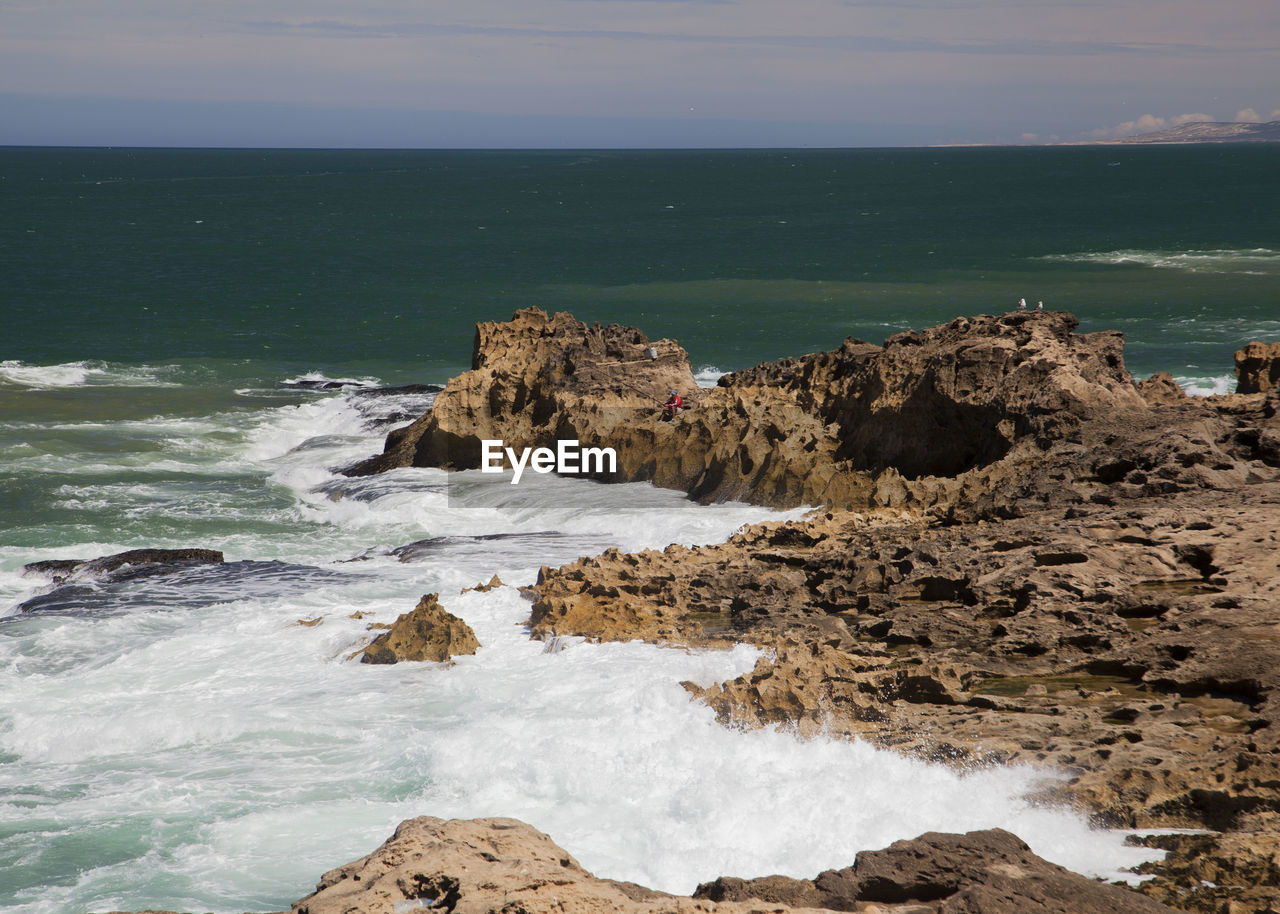 Rocks on shore by sea against sky