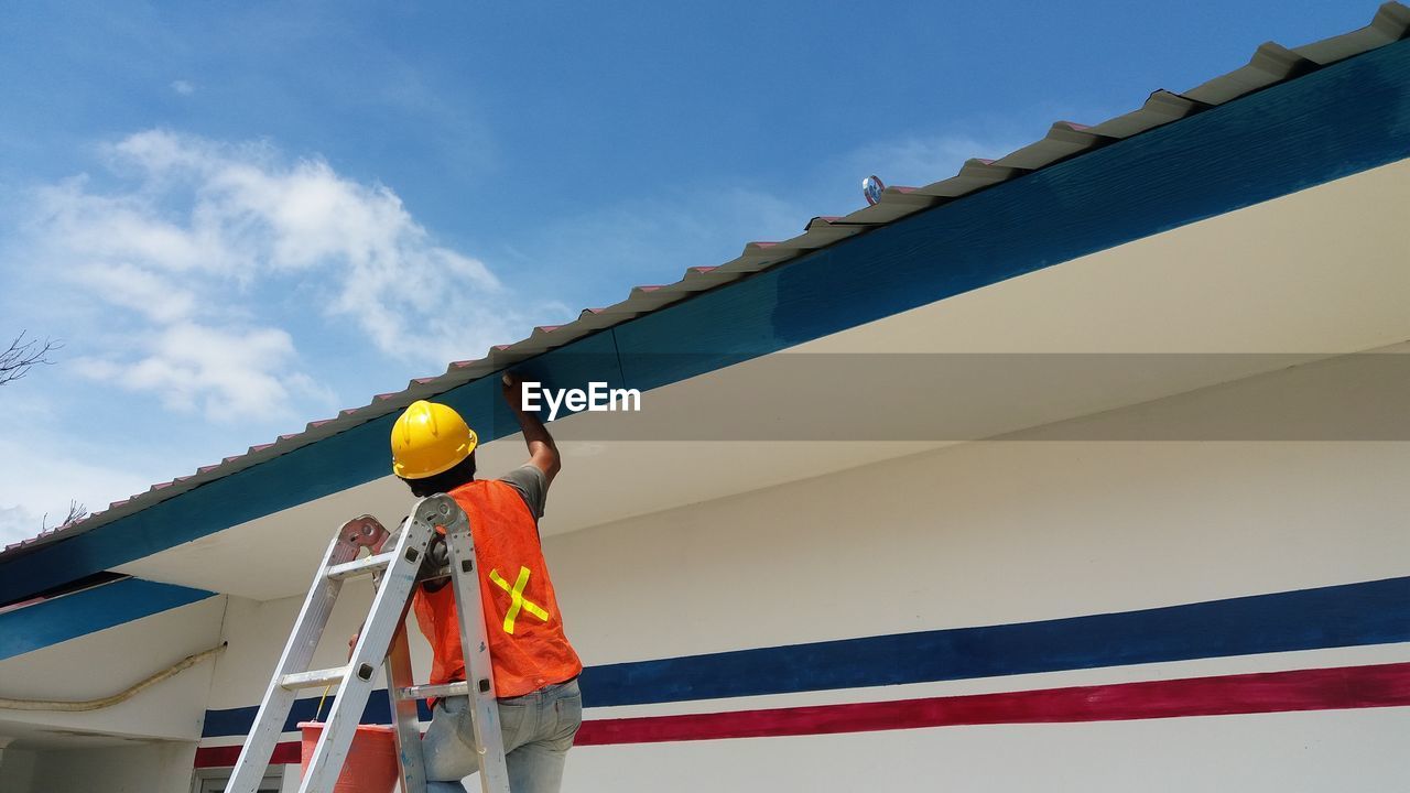Low angle view of worker working against blue sky