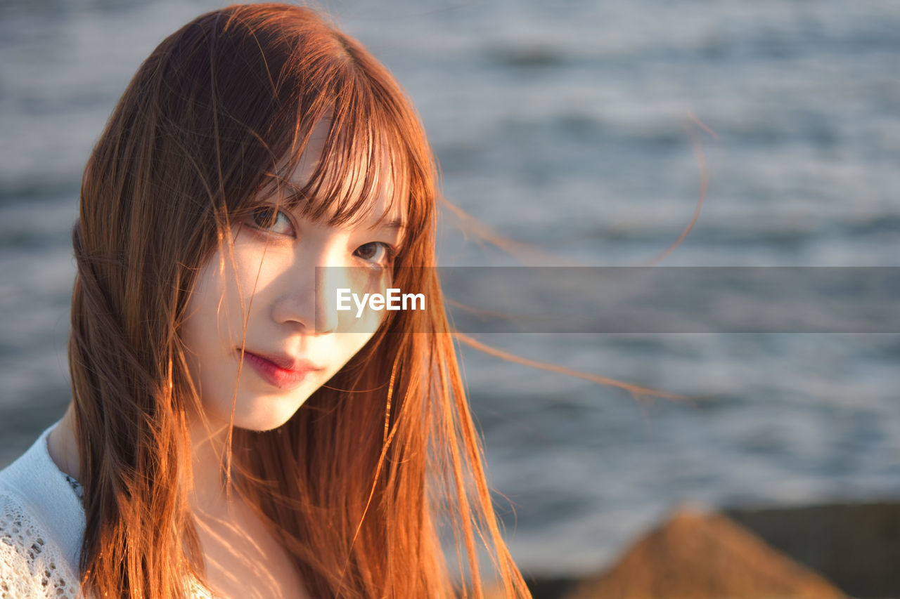 Close-up portrait of young woman with sea in background