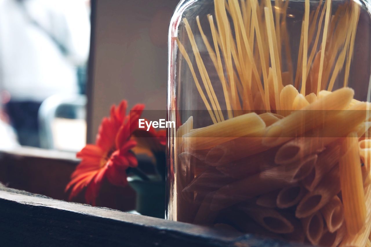 Close-up of uncooked pastas in glass by flower container 