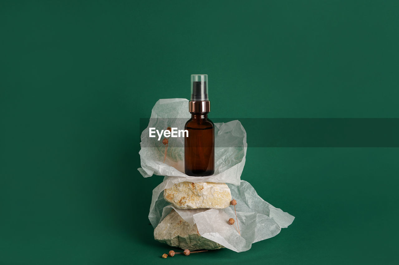 Glass bottle of moisturizing face serum, cosmetic oil on stones on green background