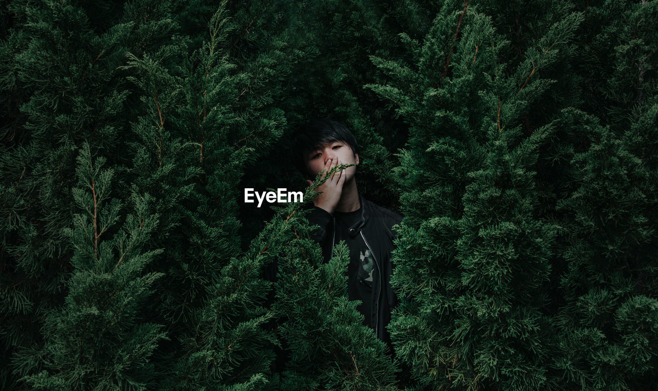 Portrait of man with hands covering mouth standing against trees