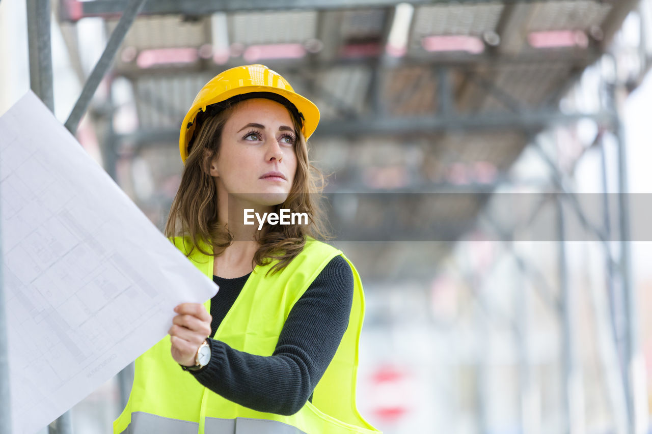 Engineer looking away while holding blueprints