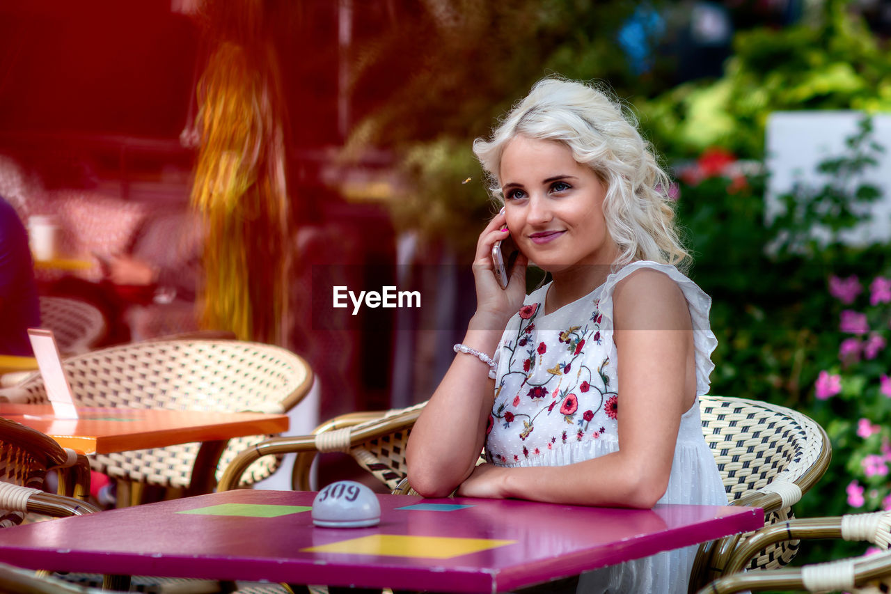 Blonde business woman talking on the phone in an outdoor cafe, the blurred foreground