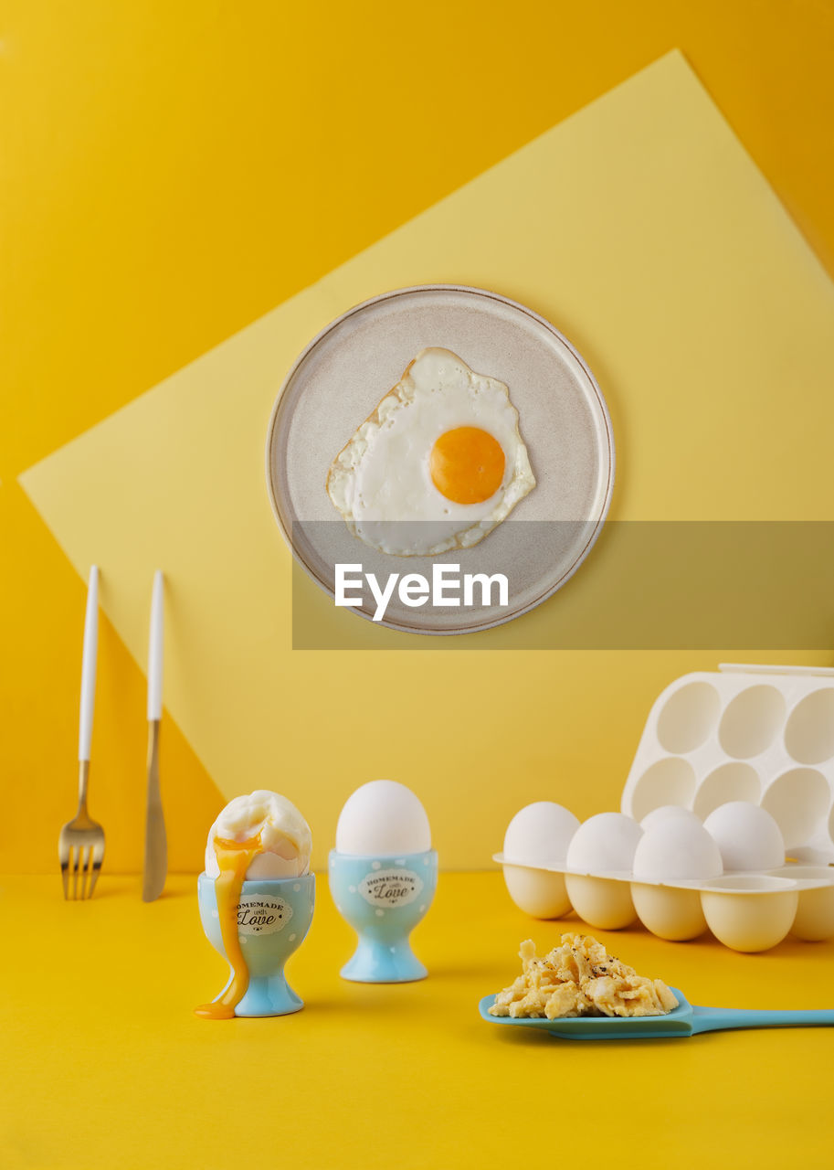 Eggs cooked three different ways on vibrant yellow background. contemporary still life