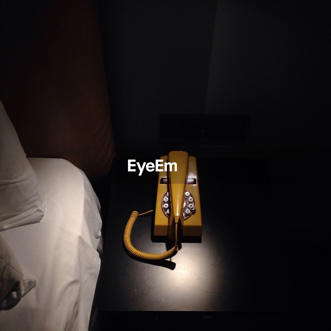 High angle view of old-fashioned yellow telephone by bed on table