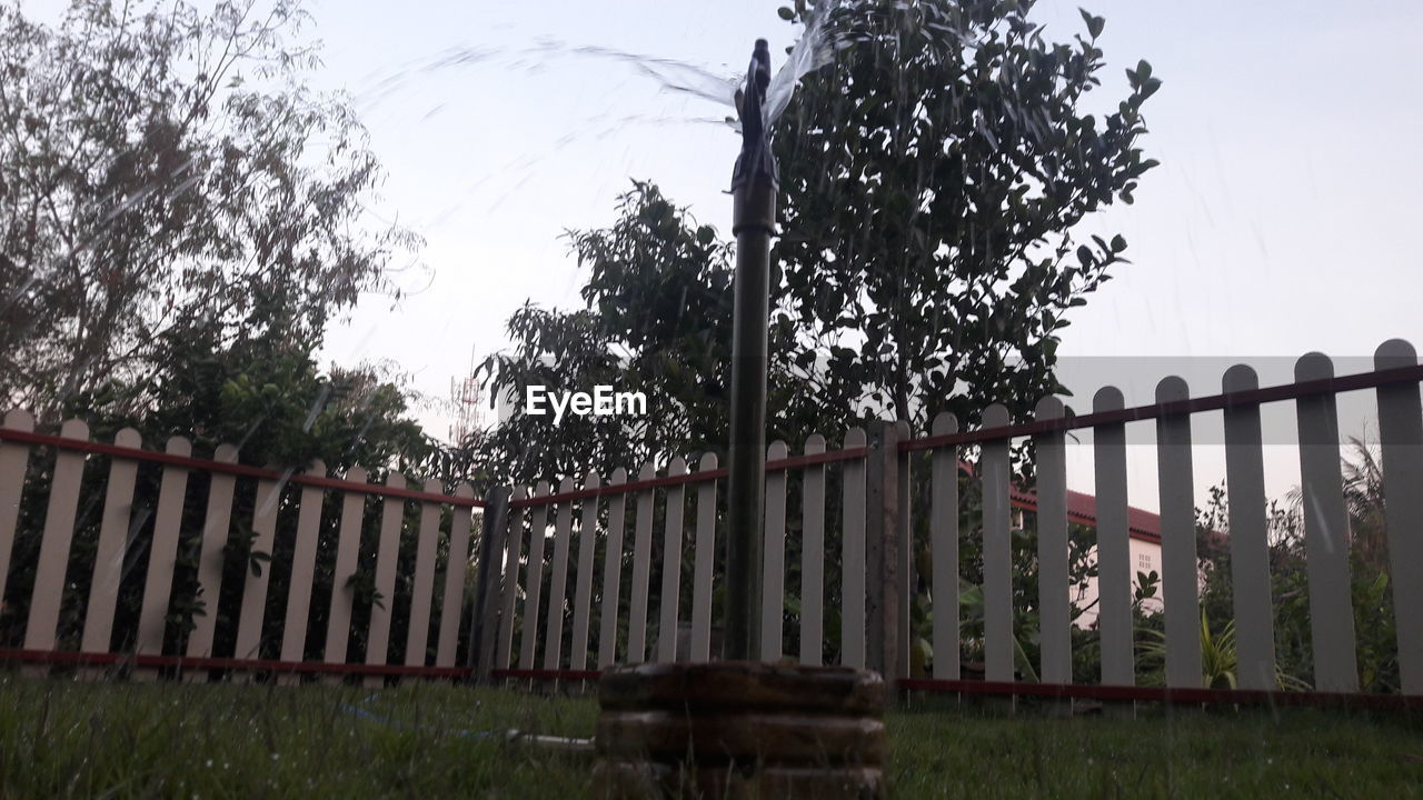 Fence by trees on field against sky