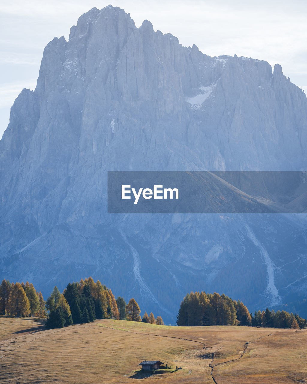 Small cottage in autumnal landscape with huge rock mountain in backdrop, vertical, dolomites