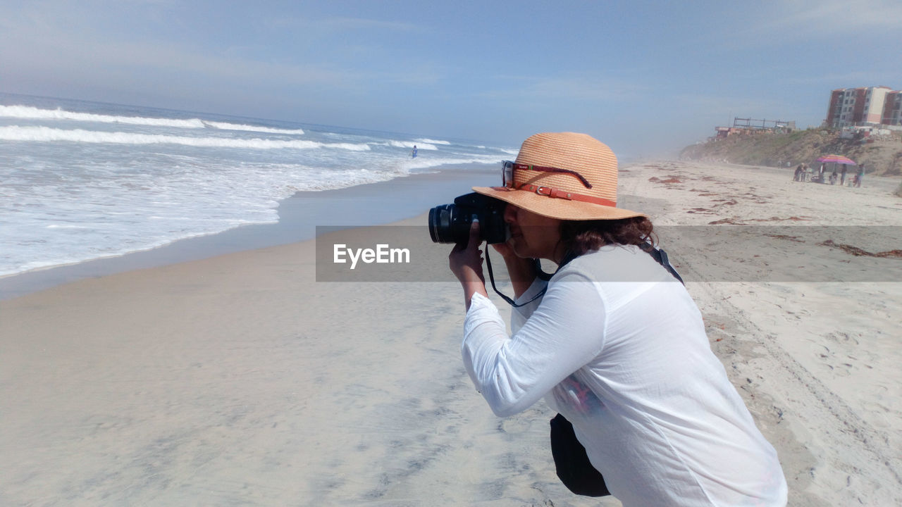 Side view of woman photographing from camera at beach 
