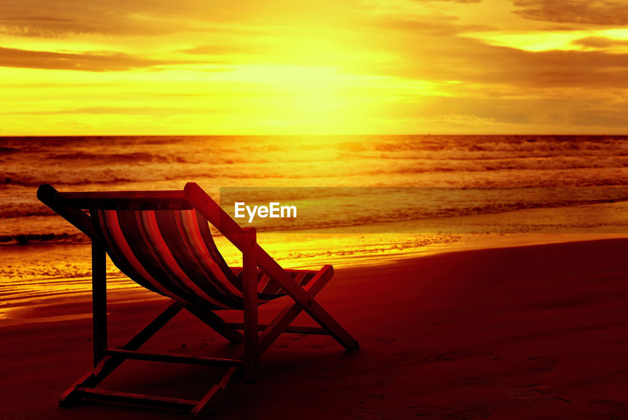 Chair on beach against sky during sunset