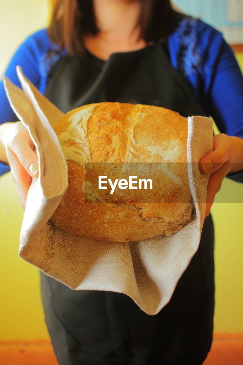 Woman holding homemade bread made with sourdough, bakery uniform, homemade bread, close-up loaf