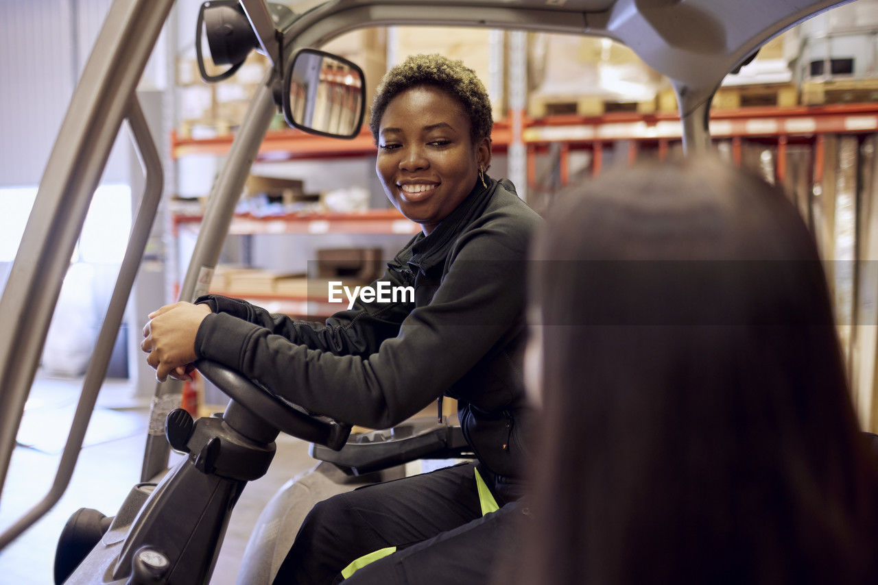 Smiling forklift operator looking at colleague in distribution warehouse