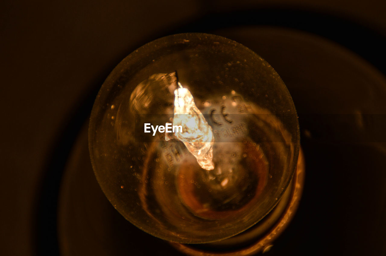 CLOSE-UP OF ILLUMINATED LIGHT BULB IN DARK ROOM