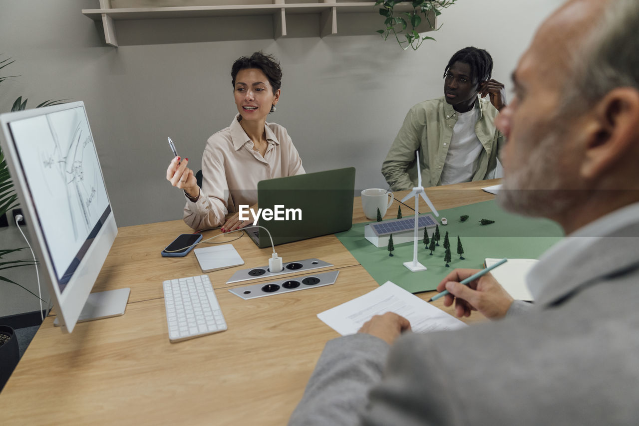 Businesswoman explaining over computer to colleagues at table in office