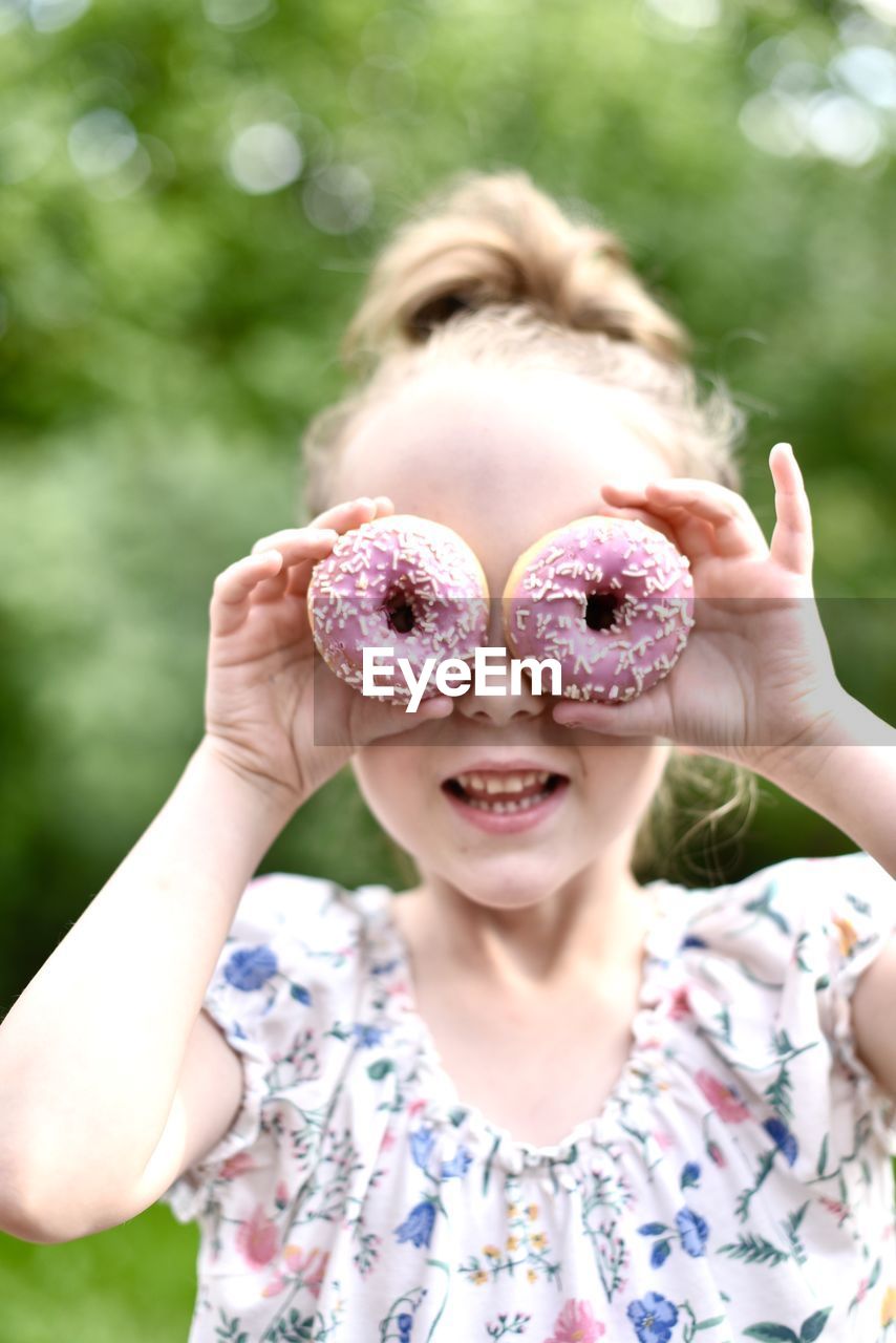 Close-up of cute girl looking through doughnuts sitting outdoors