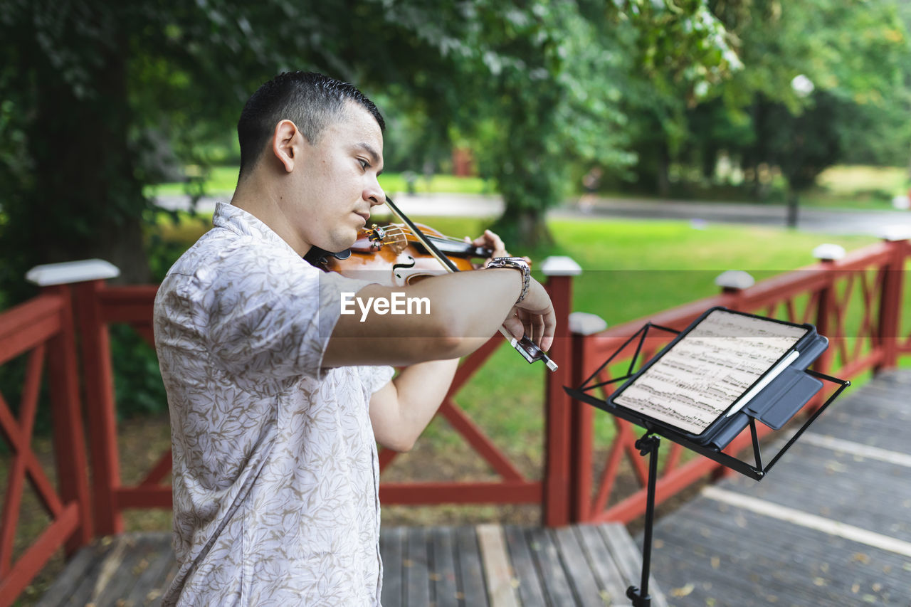 Violinist playing violin looking at sheet music in park