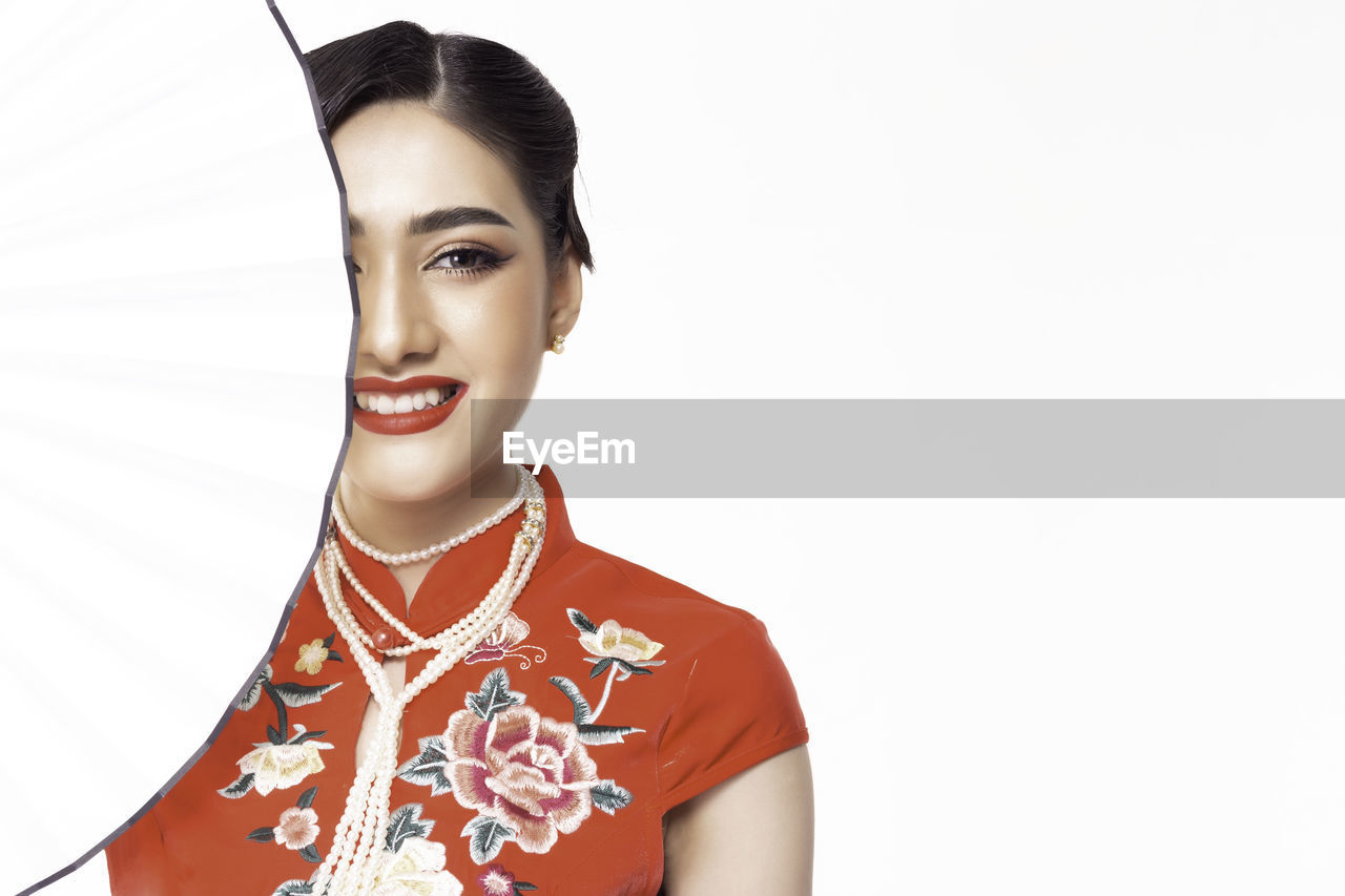 Portrait of smiling woman in red traditional clothing with hand fan against white background