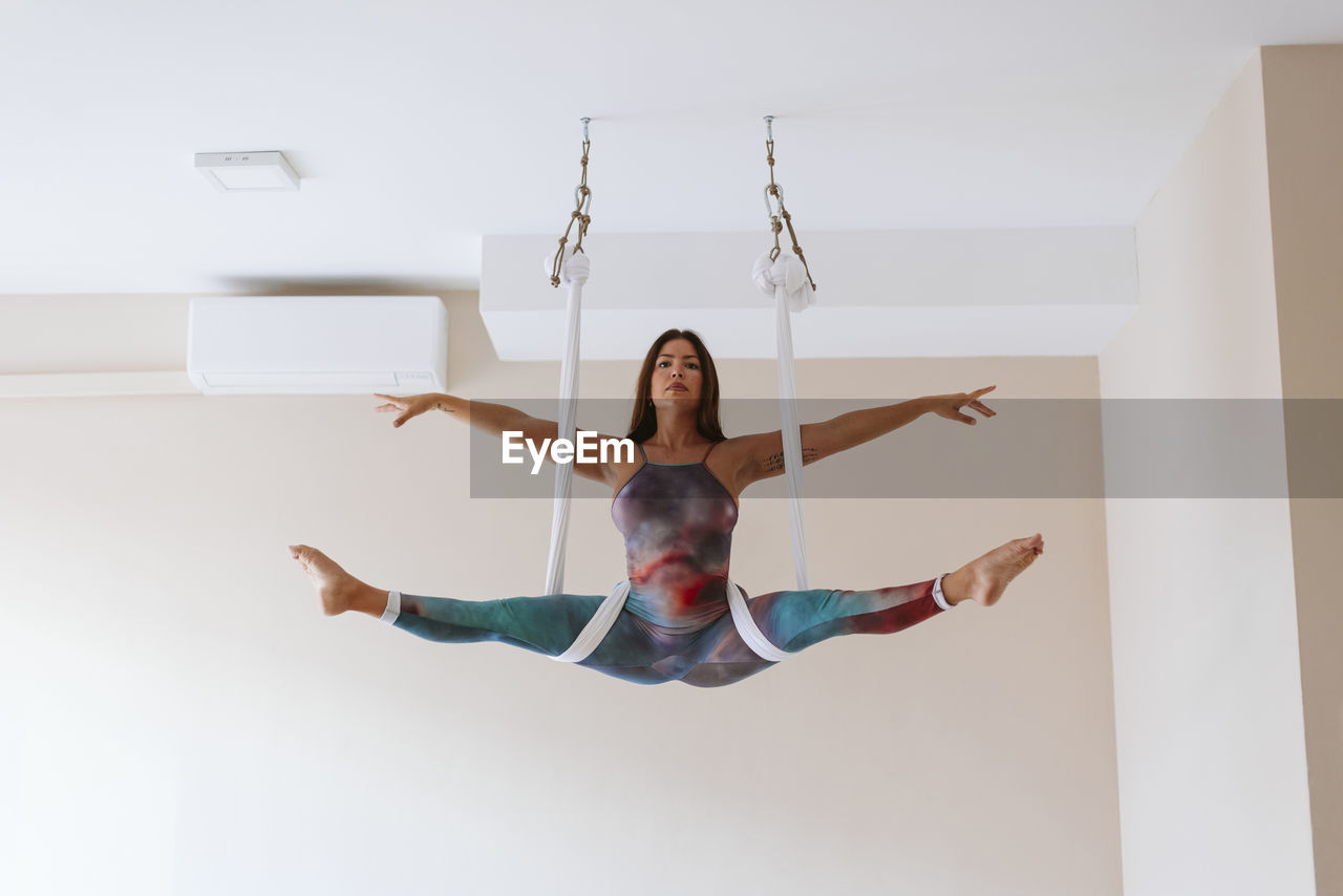 Mid adult sportswoman with arms outstretched doing splits at yoga studio