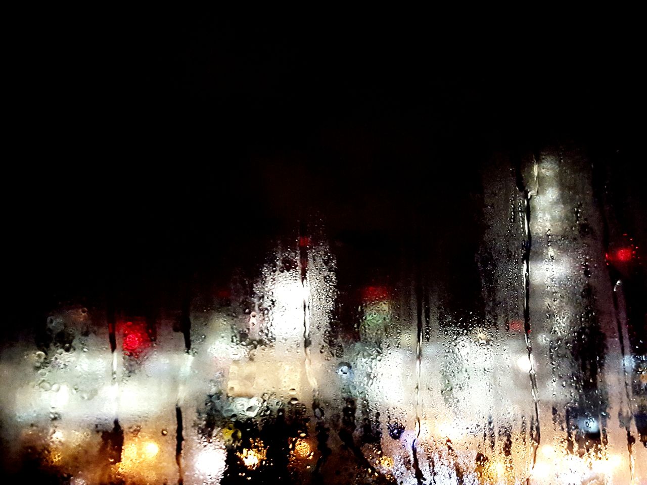 Condensed glass window against illuminated city at night