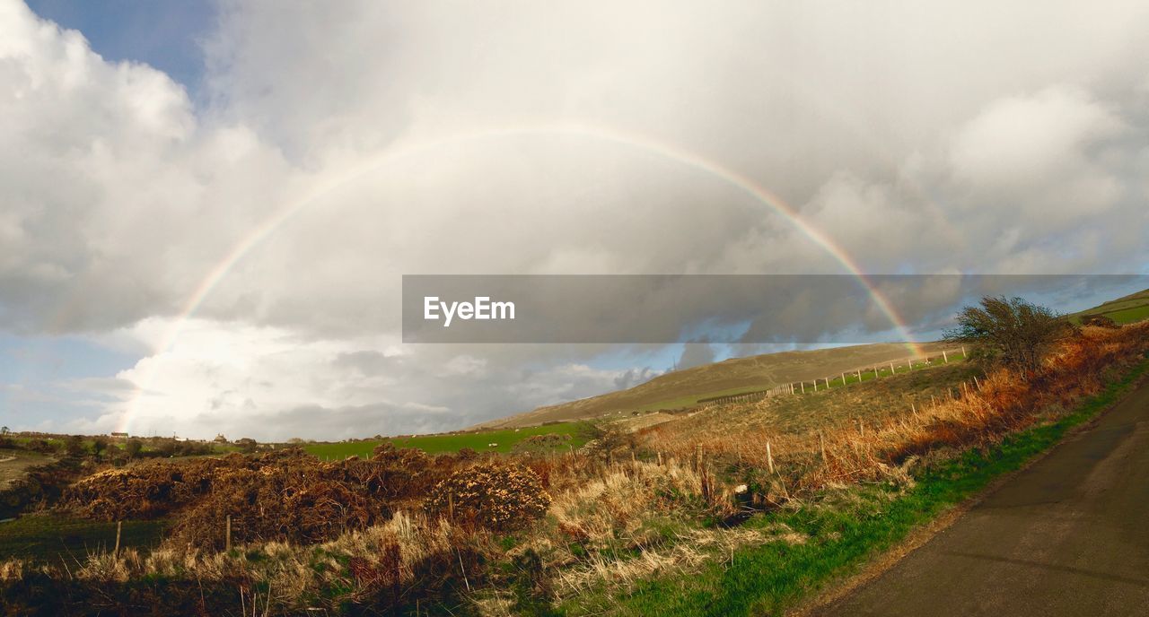 Rainbow over field against cloudy sky