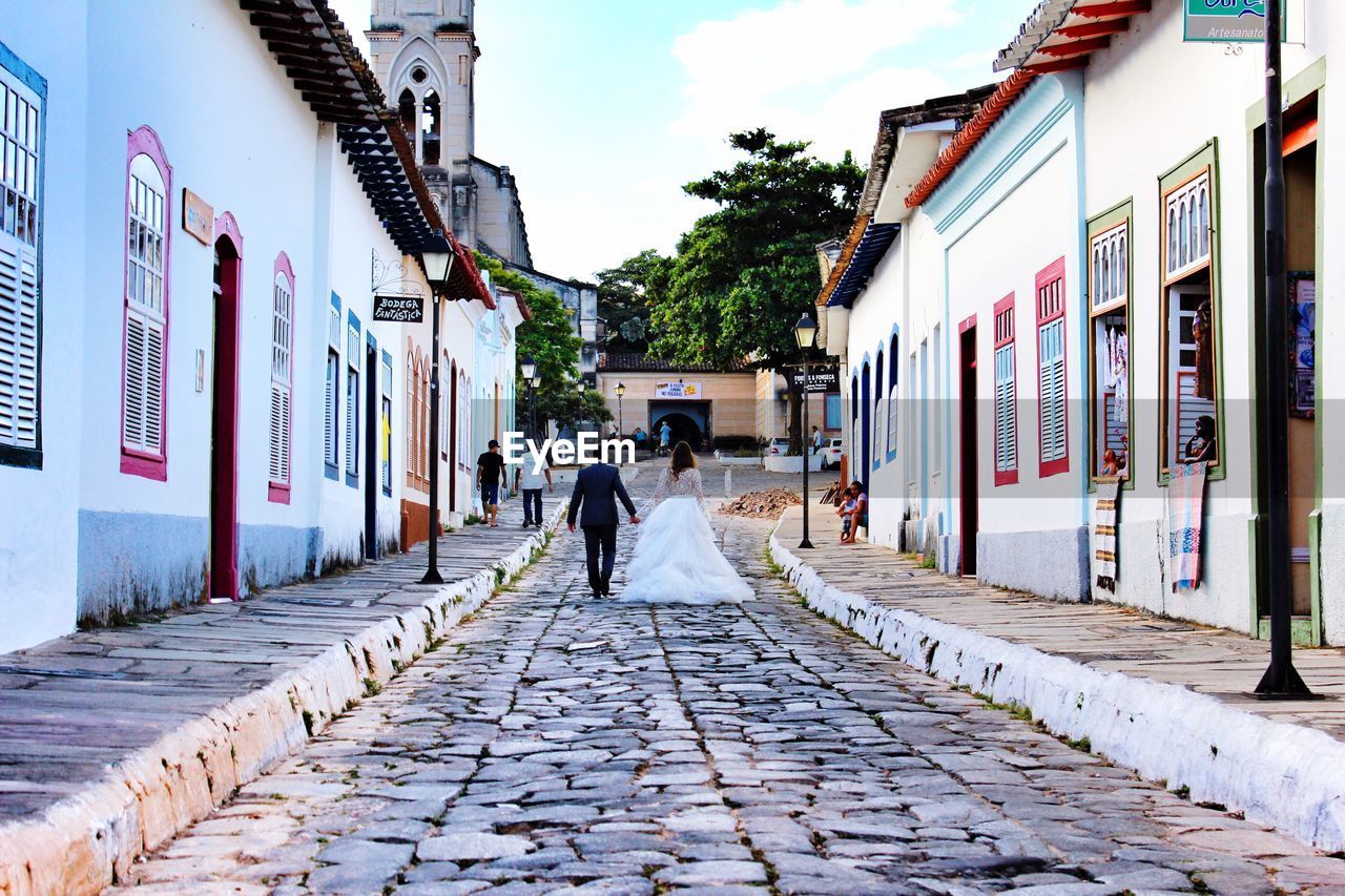 Rear view of bride and groom walking on street amidst houses