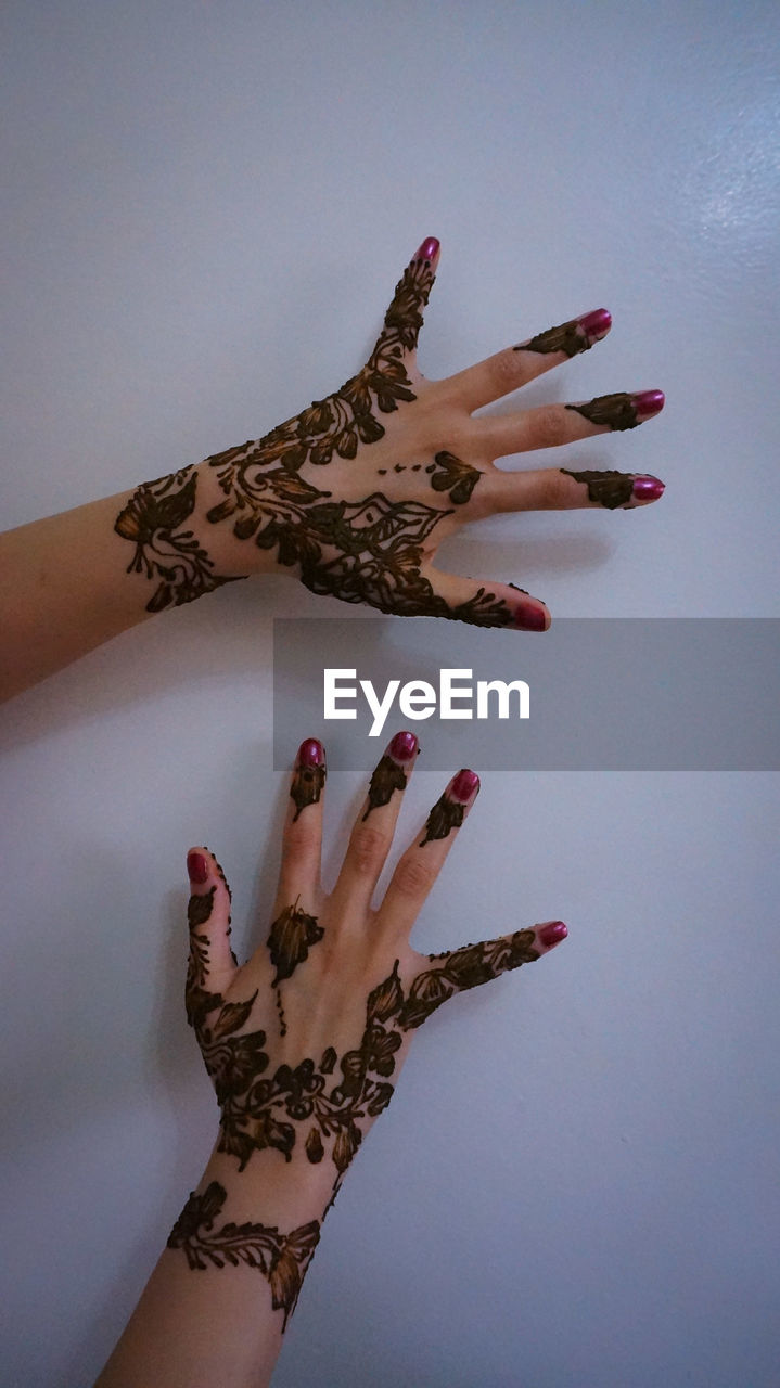 Cropped image of woman with henna tattoo against white wall