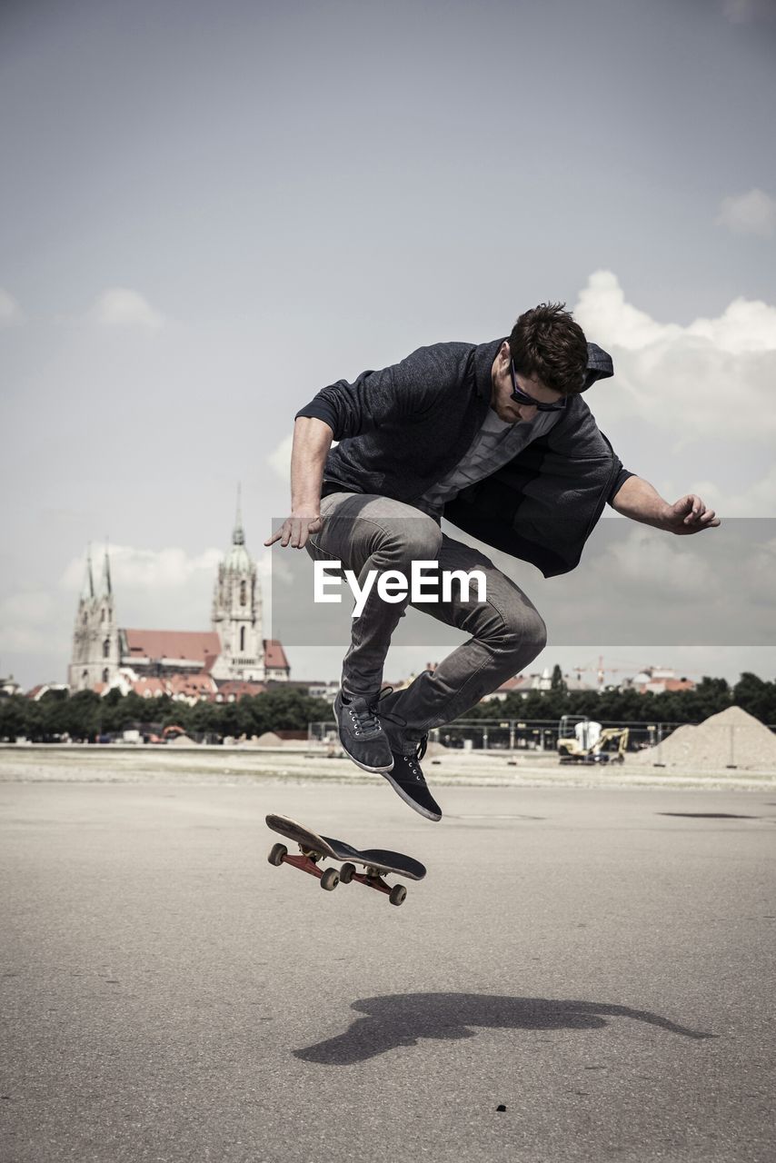 Young man doing skateboarding stunt on street against sky