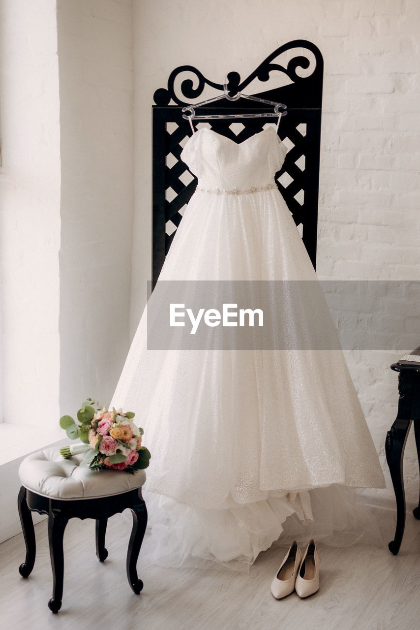 Wedding dress hanging on coat hanger against white wall