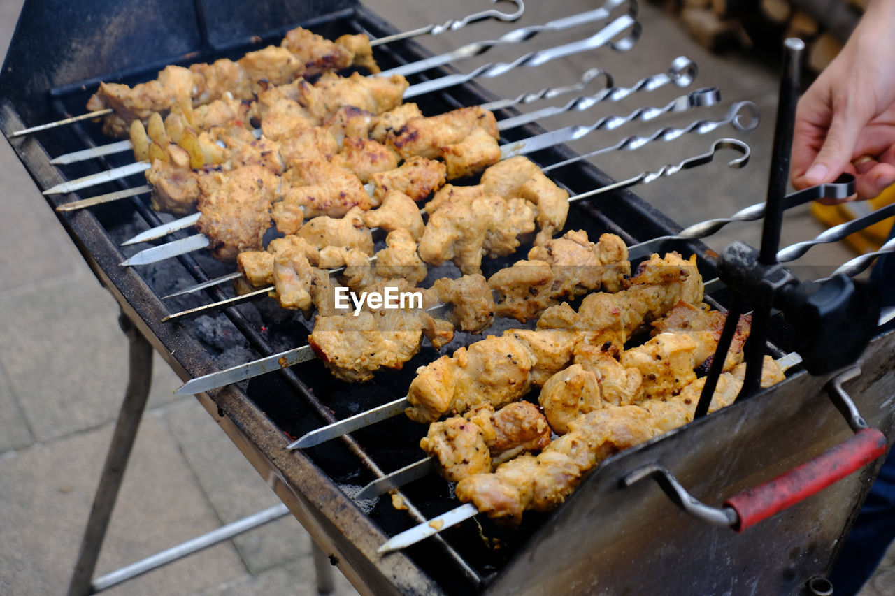 Cropped hands grilling meat on barbecue