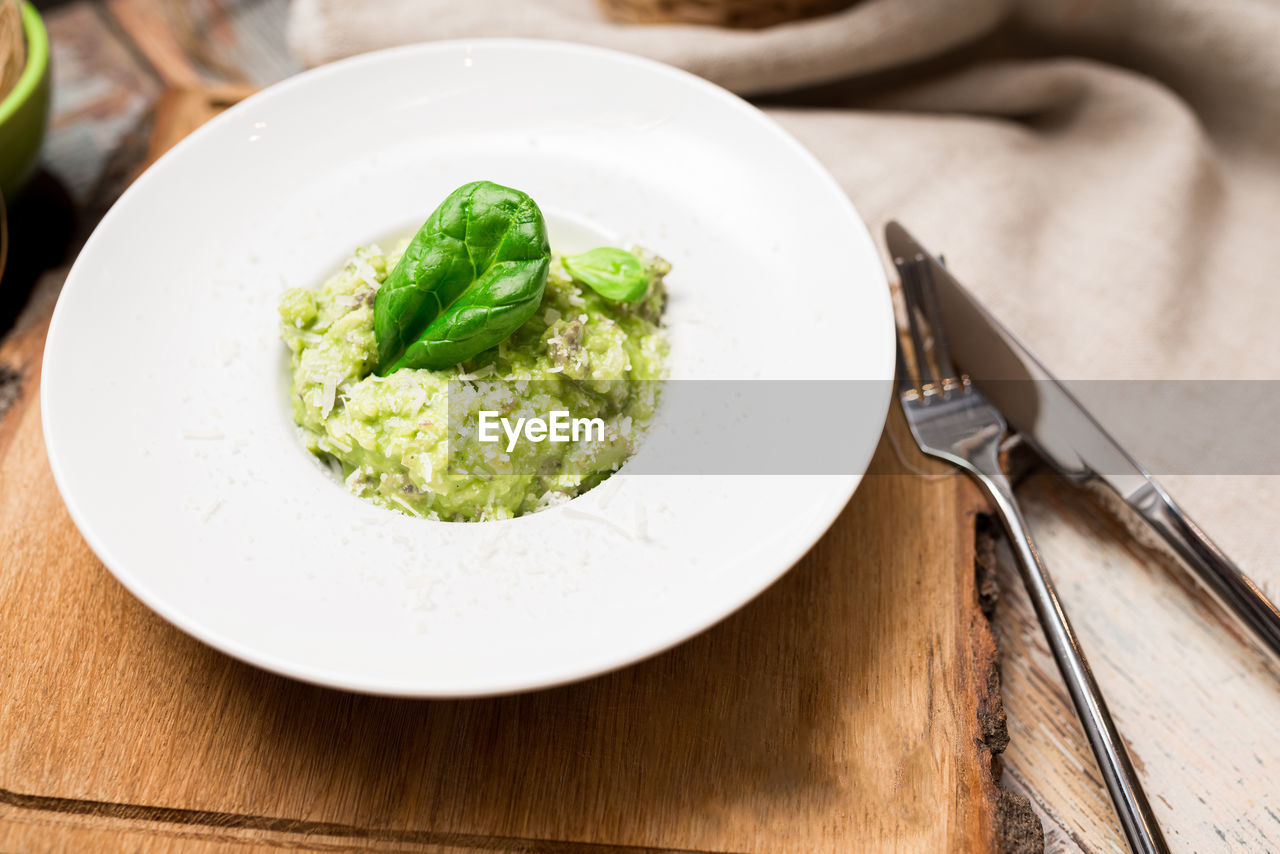 Plate serving of green risotto with basil leaves and cheese.  arborio rice with spinach and basil.