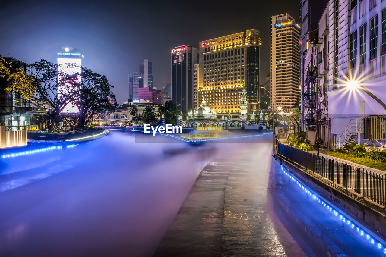 ILLUMINATED STREET AMIDST BUILDINGS AGAINST SKY AT NIGHT