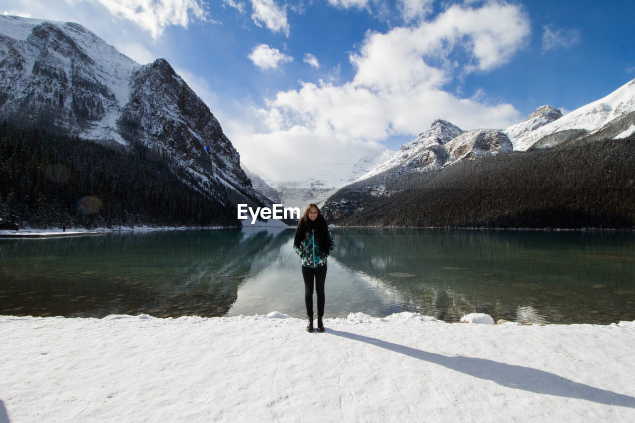 Woman standing at lakeshore against snowcapped mountain