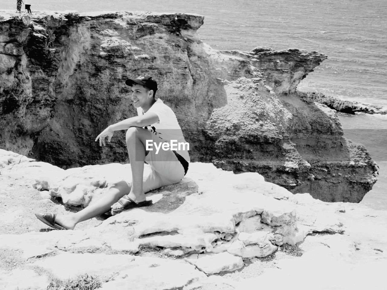 Smiling young man sitting on rock against sea at beach