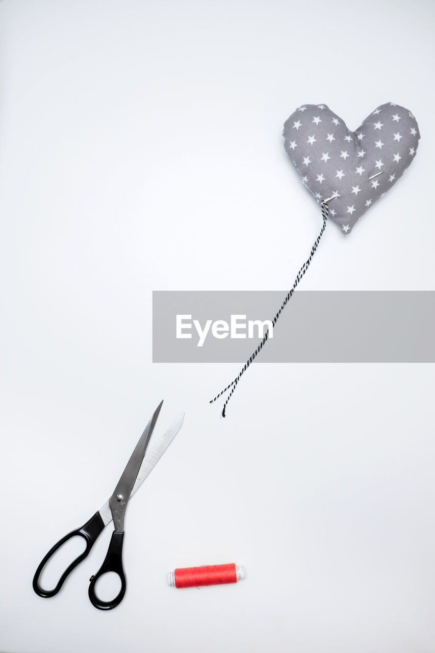 High angle of scissors, needle, heart shaped pillow and yarn. imitating banksy love is i. t. bin.