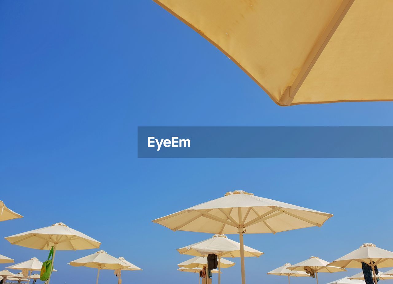 Low angle view of beach umbrellas against clear blue sky