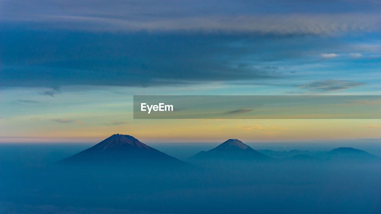 Merbabu, merapi, and prau mountain peak in hazy foggy morning with clouds and sunrise in horizon