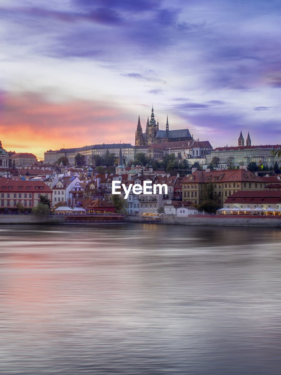 City by river against sky during sunset