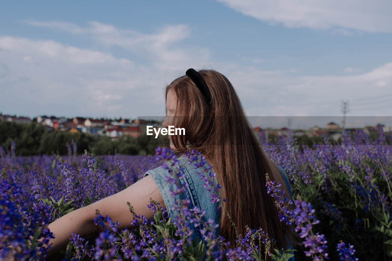 REAR VIEW OF WOMAN WITH PURPLE FLOWERS ON FIELD