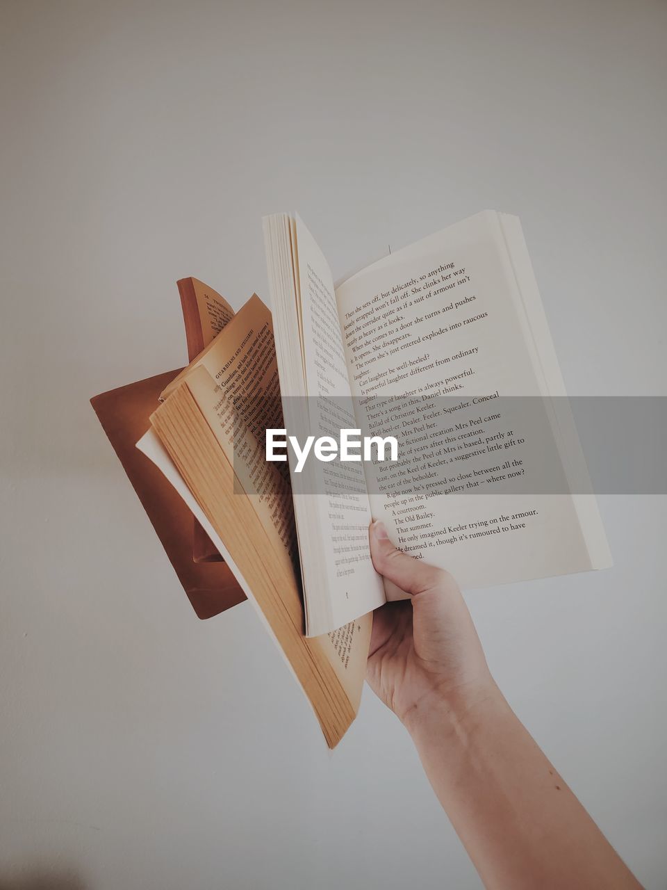 Cropped hand holding books against grey background 