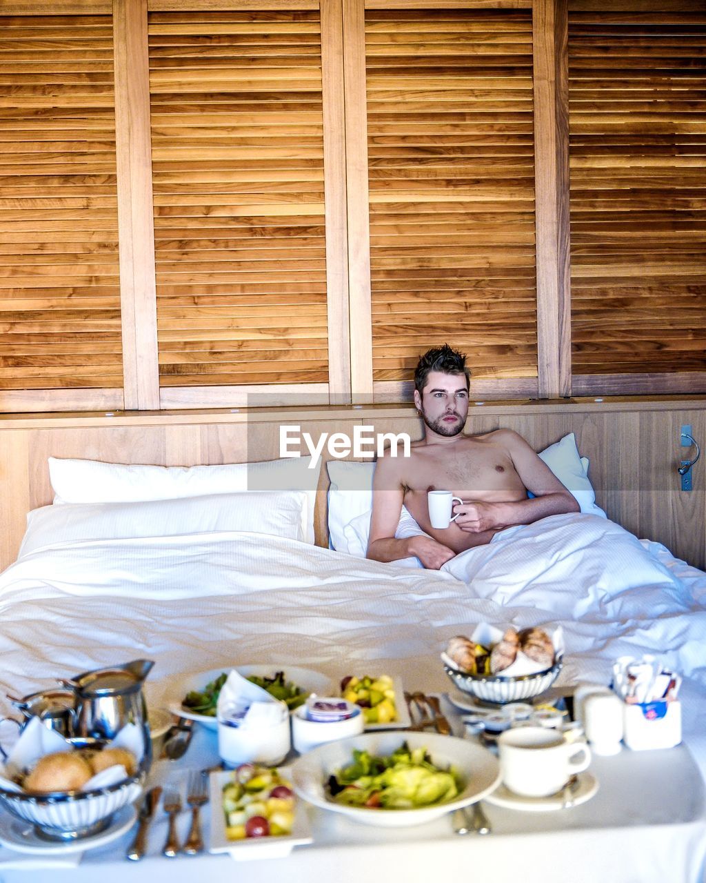 Shirtless man with coffee on bed at home