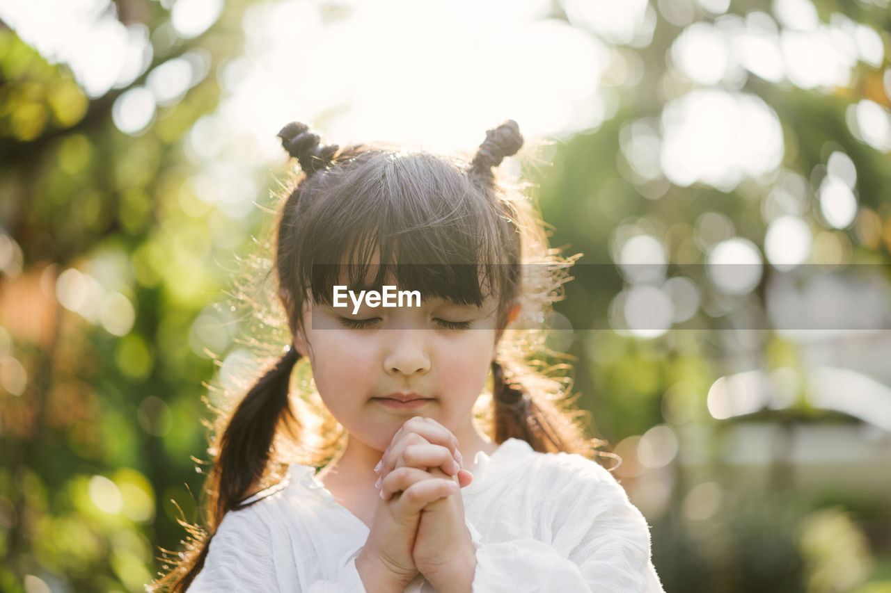 Cute girl praying while standing in park