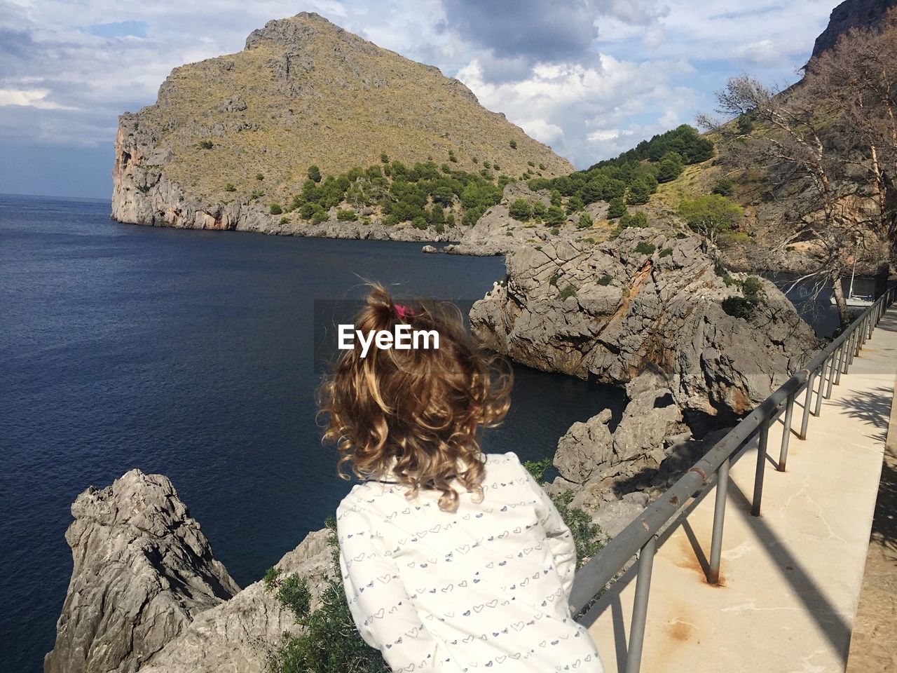 Rear view of girl standing by railing at torrente de pareis against cloudy sky