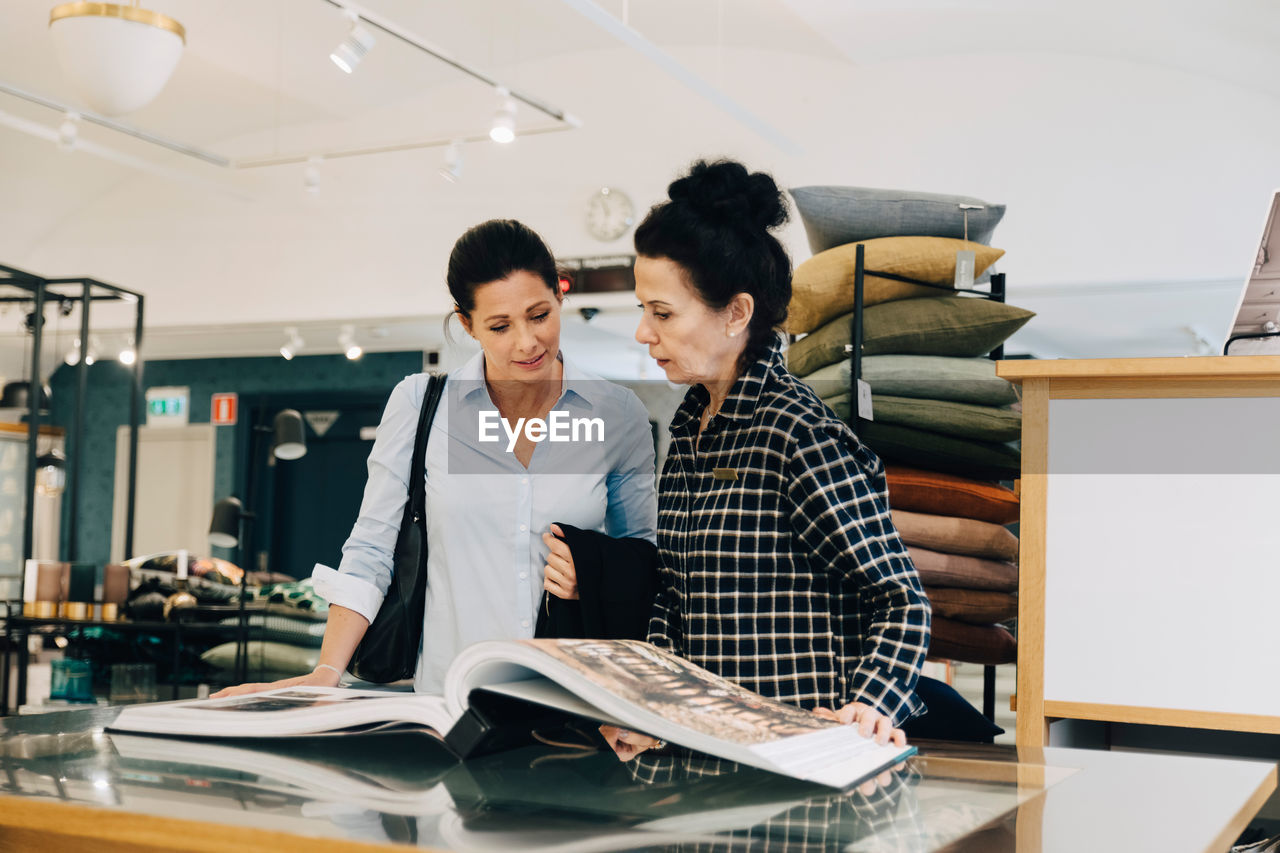 Woman assisting customer choosing wallpaper sample in store